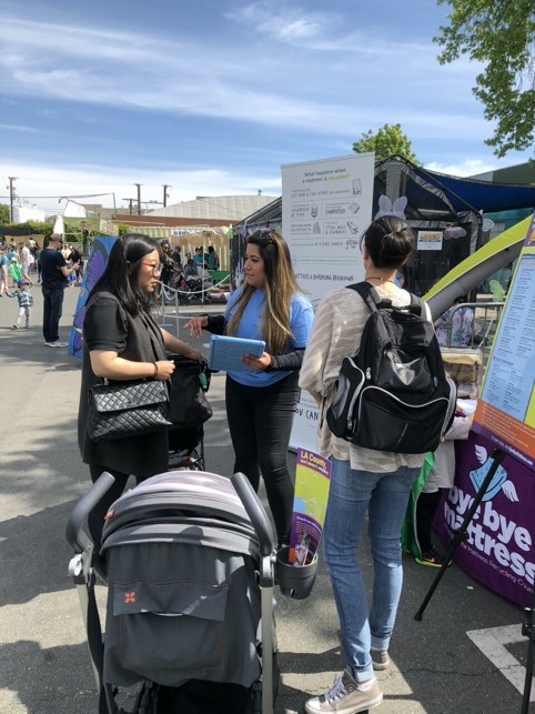 A woman talking to another woman stopping by the event booth while she has an IPad in her hand with the survey.