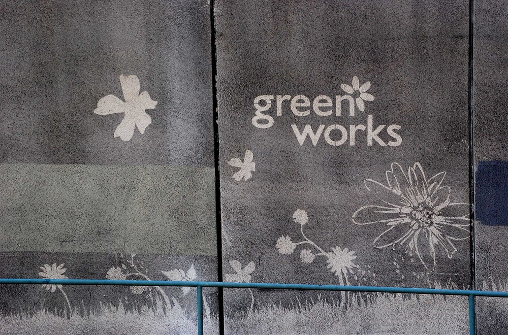 Dirty pavements with a stencil of clean pavement showing the Green Works logo and a grass and flowers design